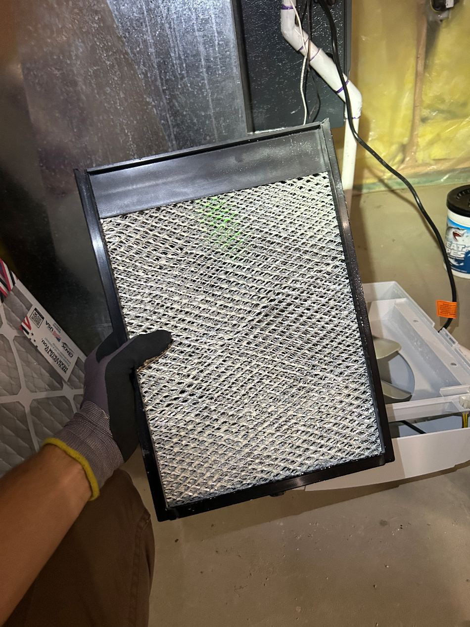 A fresh humidifier water panel held at an open whole-home humidifier during a furnace visit